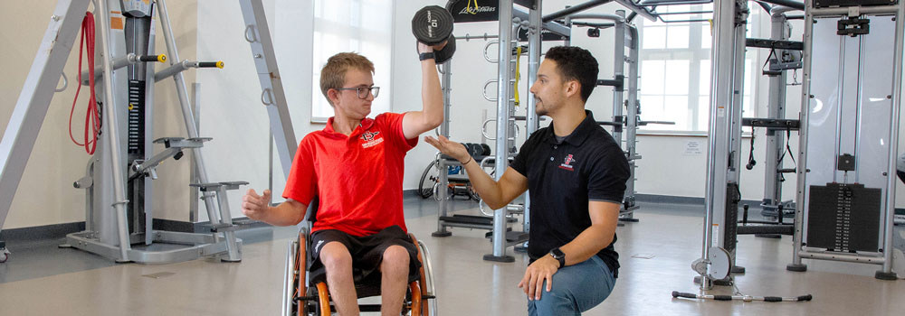 Adapted Athletics Strength and Conditioning Coach guiding a student with a dumbe