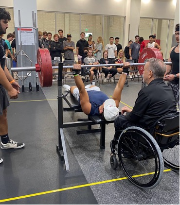 Weightlifting competitors bench pressing as spectators observe