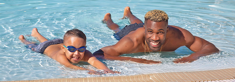 Boy learning to swim in pool with father