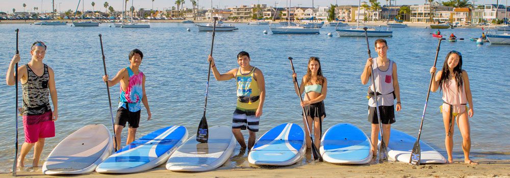 Peaple standing next to paddle boards on the beach