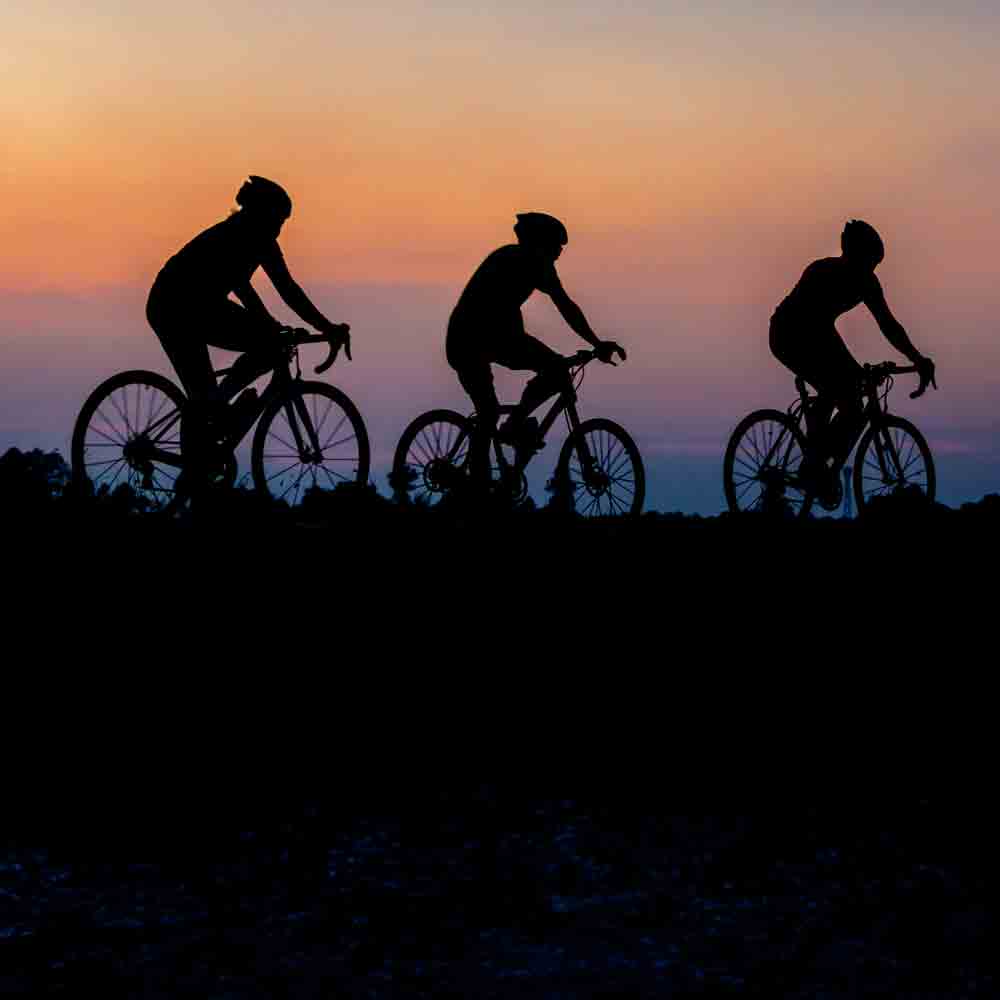 Three cyclists silhouetted on bikes at sunset