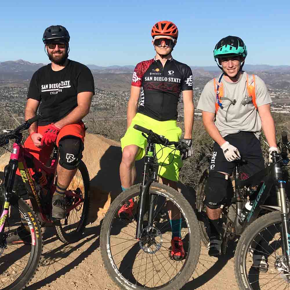 Three smiling cycling club members on their bikes on top of the mountain