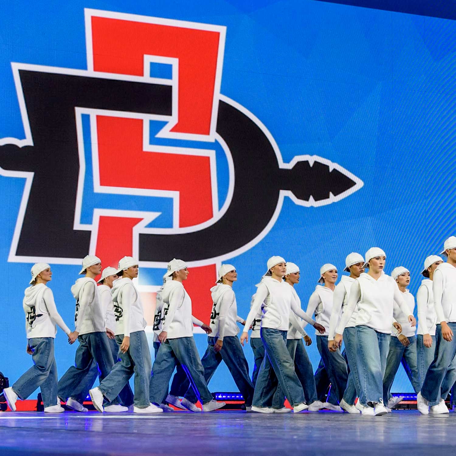 Dance Team walking onto a stage with Aztec Athletics logo background