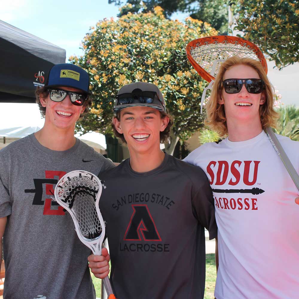 Three smiling men's lacrosse club members at a recruiting event
