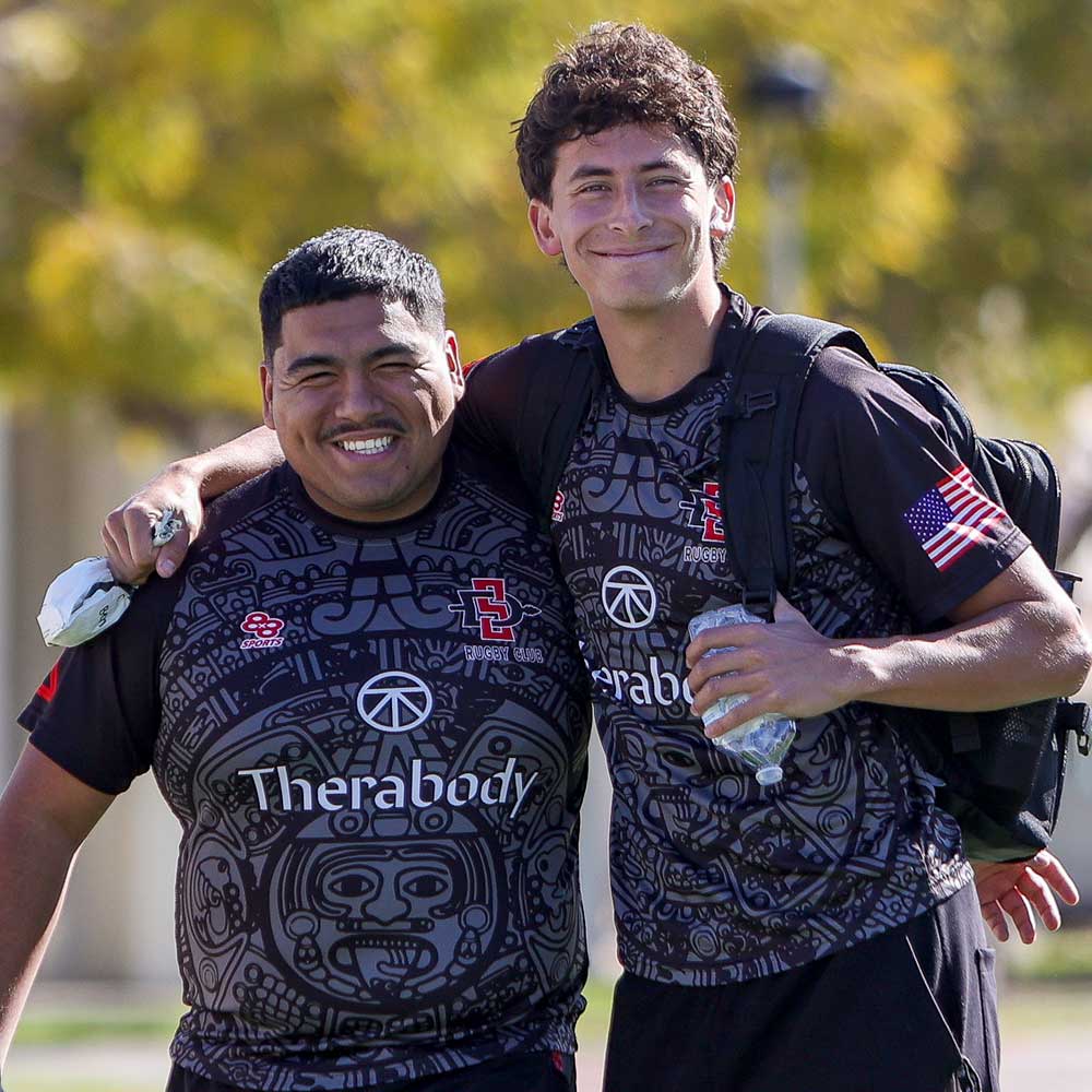 Two smiling men's rugby club members eating watermelon after the game