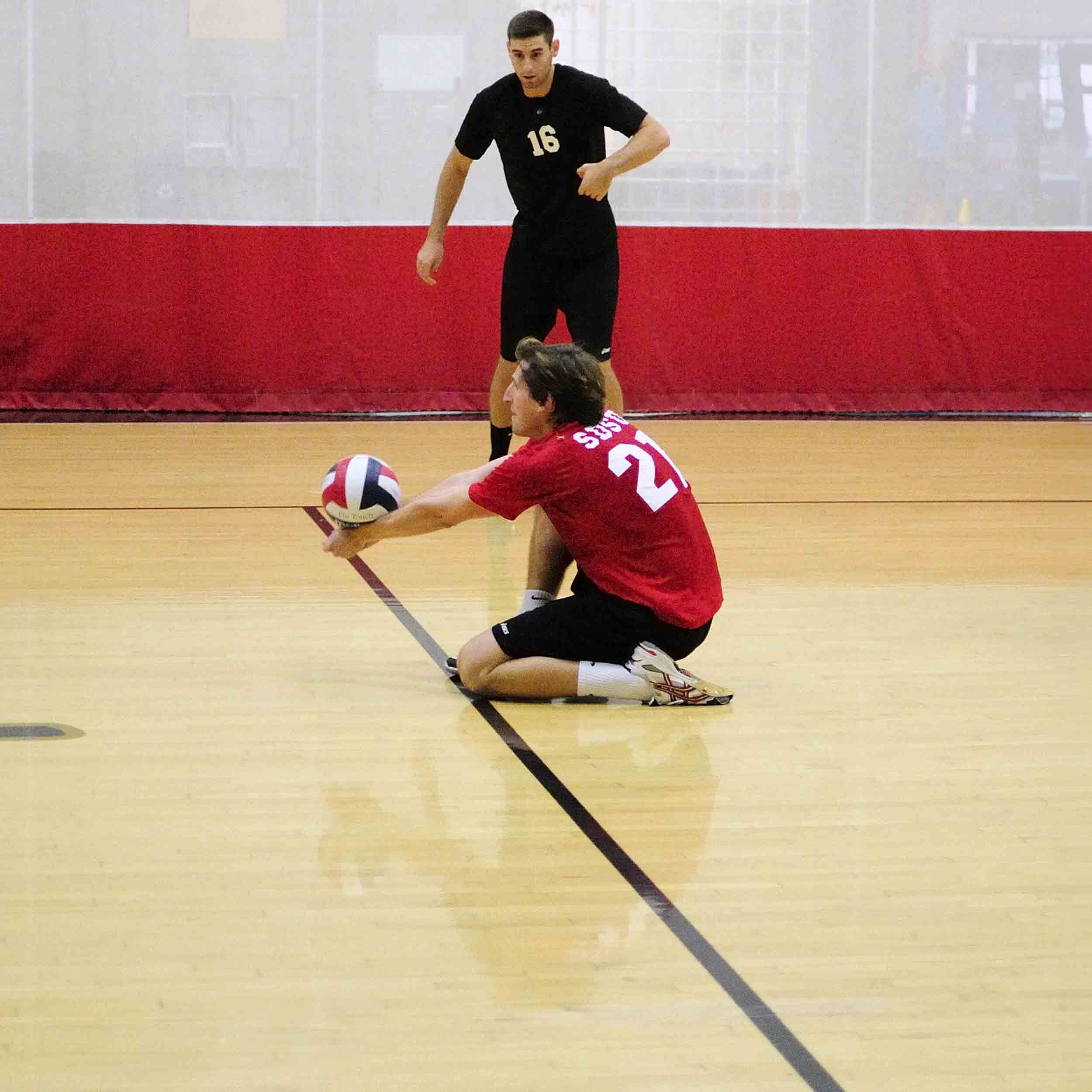 Men's Volleyball player kneeling on court hitting the ball