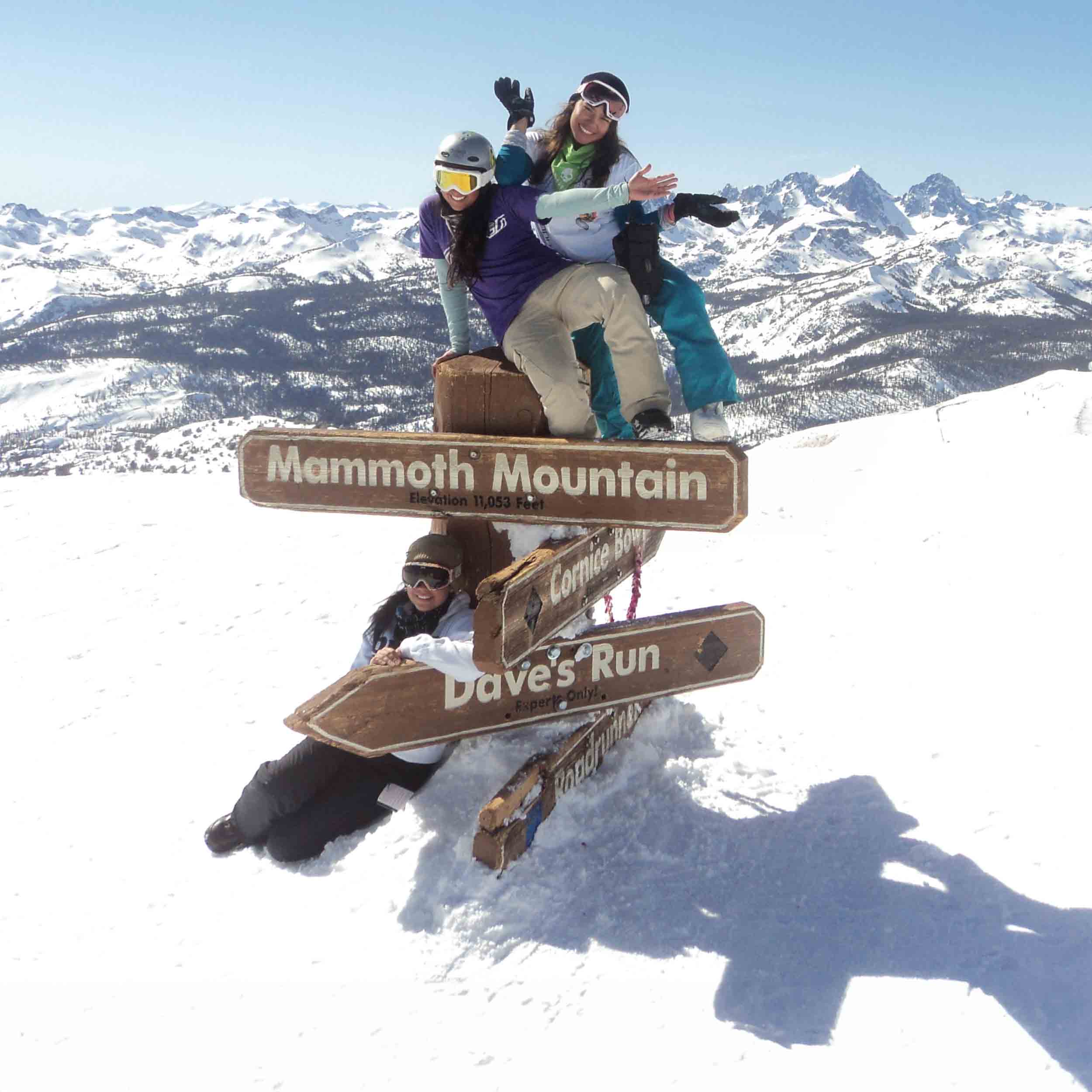 Ski and Snowboard team mebers posing in front of a directional sign on snow