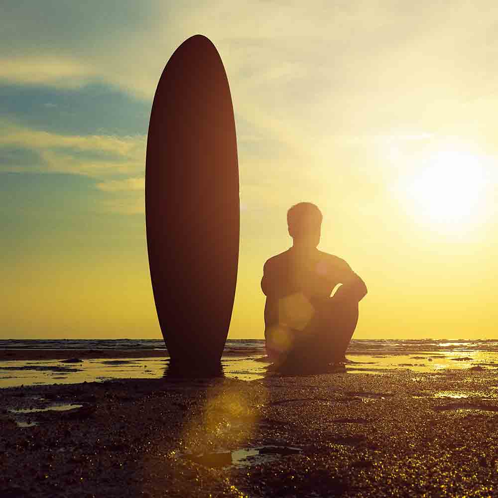 Surfer sitting on the beach with his surfboard during a sunset