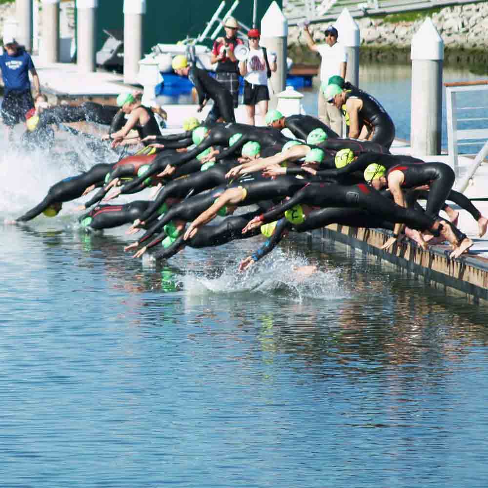 Group of triathlon members jumping into the water from the dock