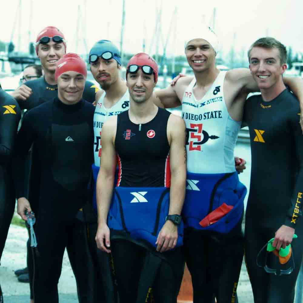 Group of triathlon members in wetsuits posing for a photo 