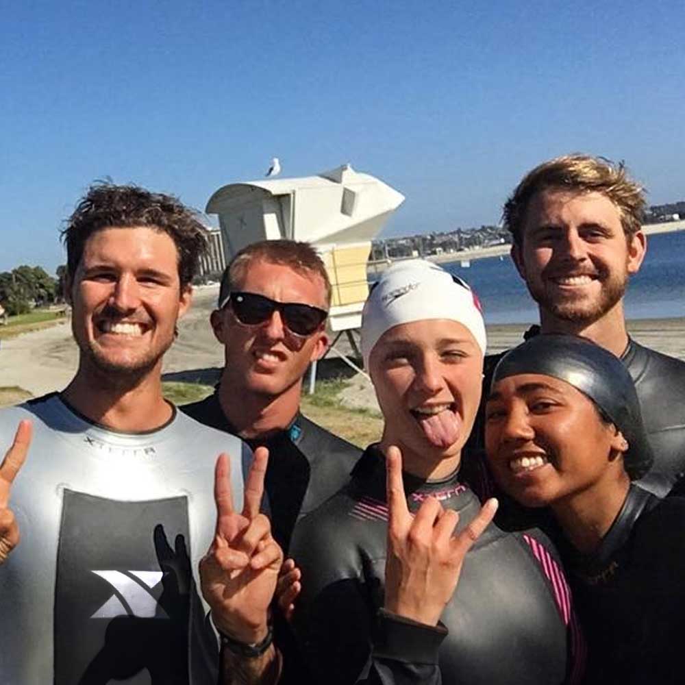 Five smiling triathlon club members in wetsuits at the beach