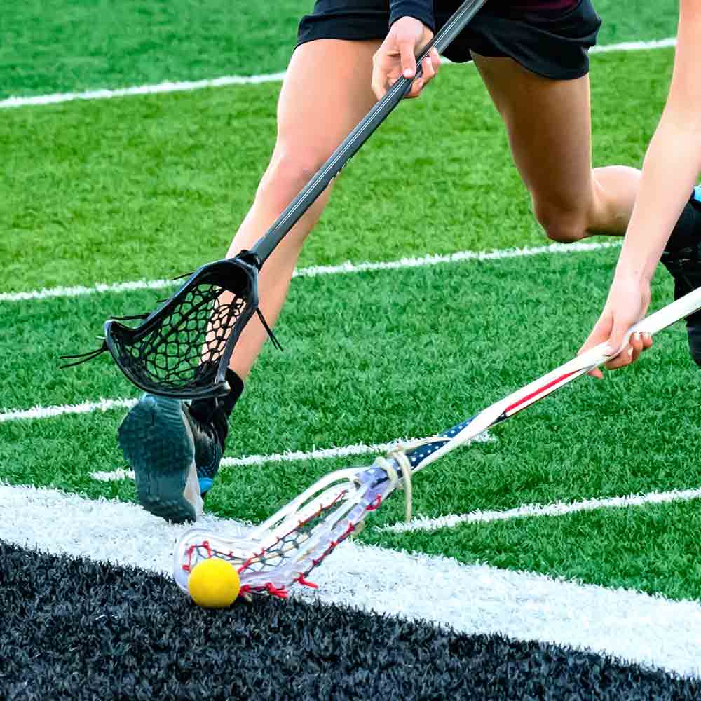 SDSU Women's Lacrosse playing lacrosse on a field, holding a lacrosse stick picking up a ball.

