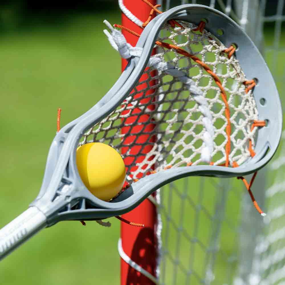 Lacrosse stick with a ball next to the goal net.

