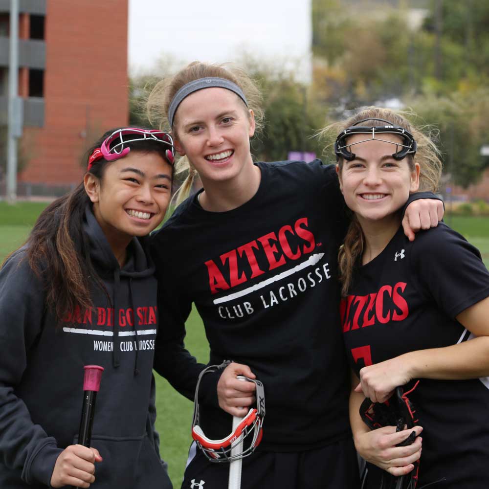 Three smiling women's lacrosse members at a practice