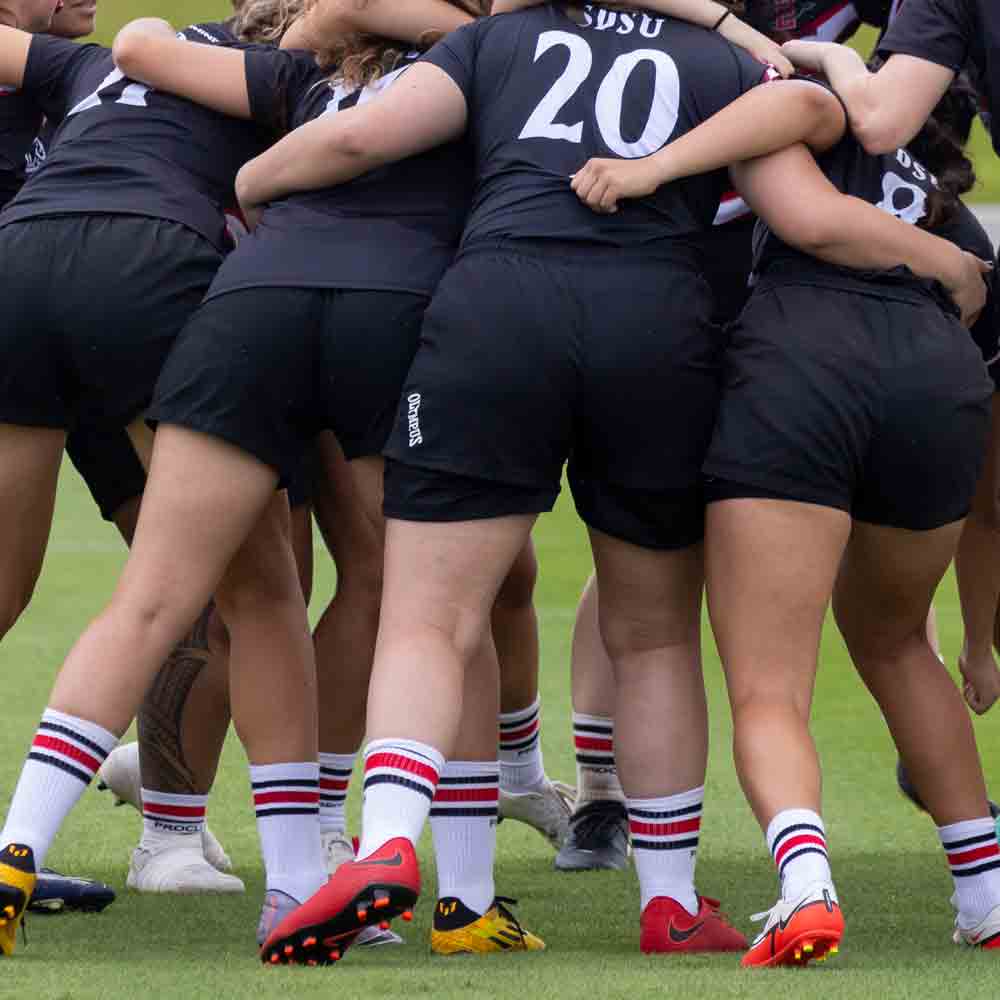 SDSU women's rugby players in a huddle during a game
