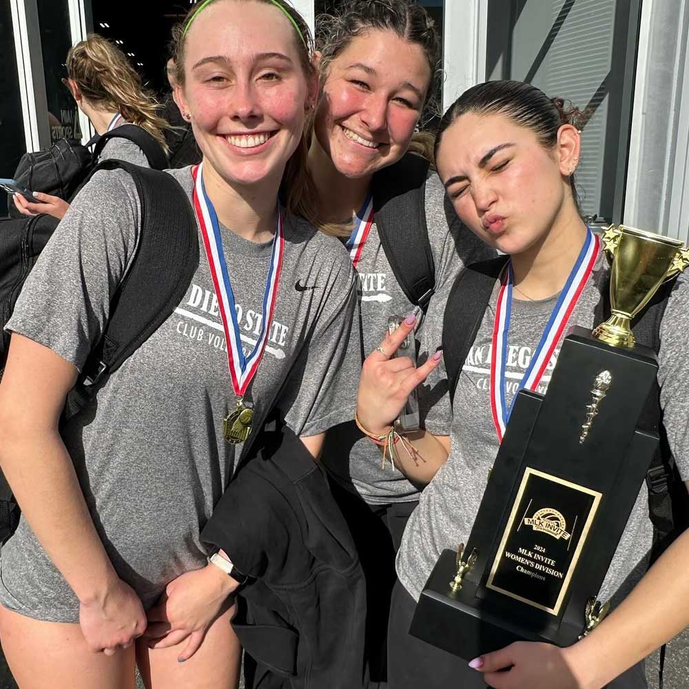 Three smiling volleyball club members, holding a trophy